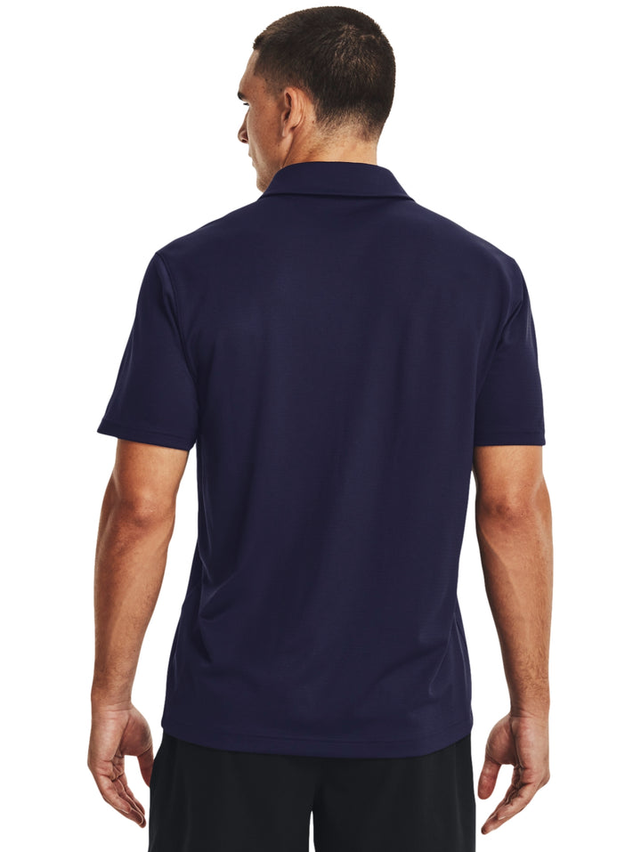 Hombre vistiendo polo deportivo Under Armour de color azul marino con logotipo blanco en el pecho.