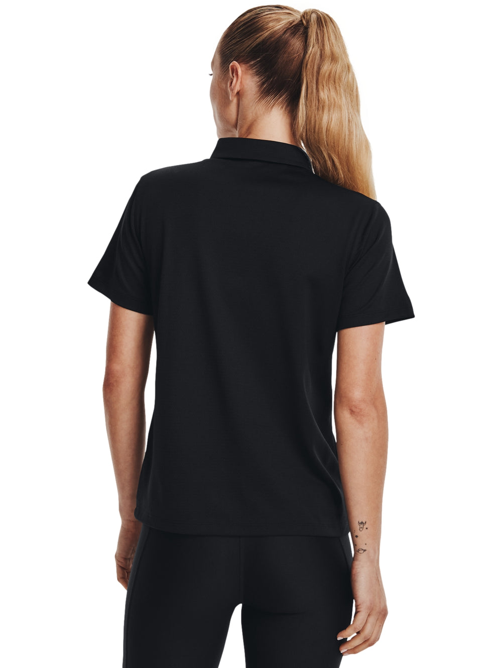 Mujer vistiendo polo deportivo Under Armour de color negro con cuello y manga corta.