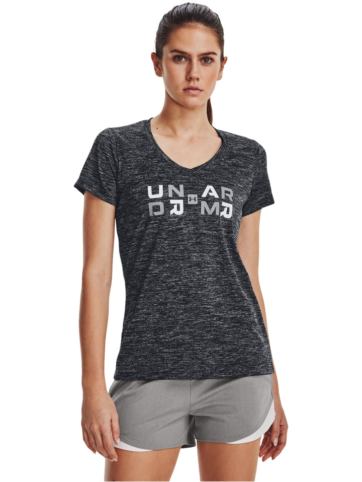 Mujer vistiendo playera deportiva Under Armour color negro jaspeado con gráfico blanco y shorts grises.