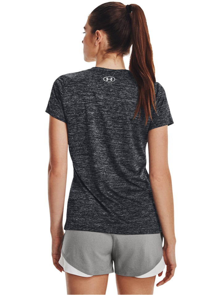 Mujer vistiendo playera deportiva Under Armour color negro jaspeado con gráfico blanco y shorts grises.