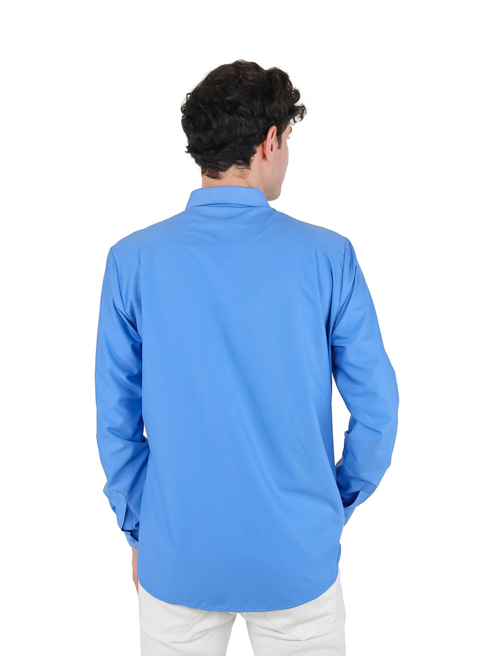 Hombre vistiendo una camisa azul de manga larga con botones y pantalones blancos sobre fondo blanco.