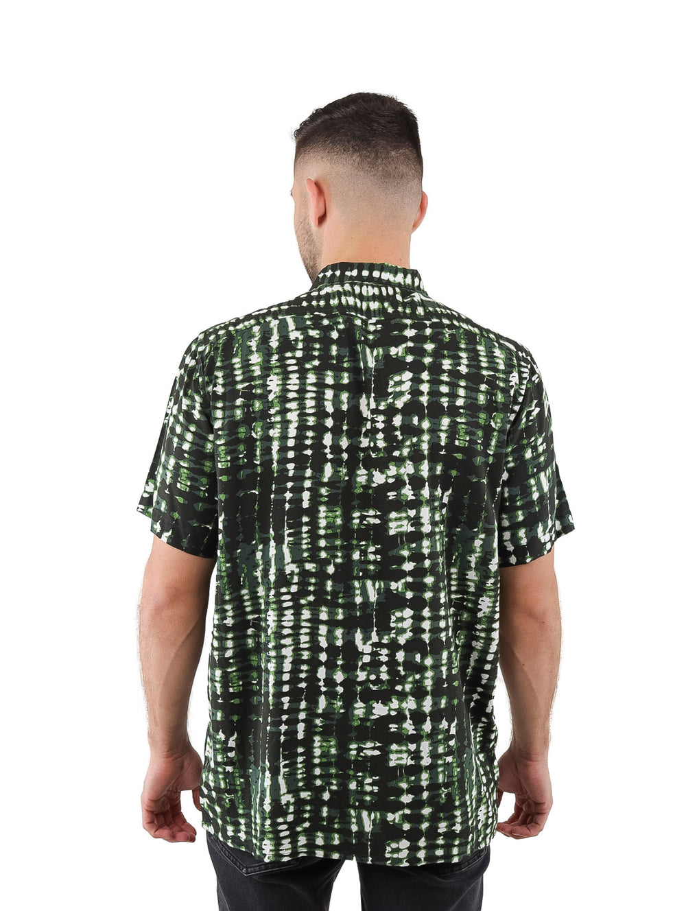 Hombre vistiendo camisa de manga corta con estampado abstracto en tonos verde, negro y blanco.