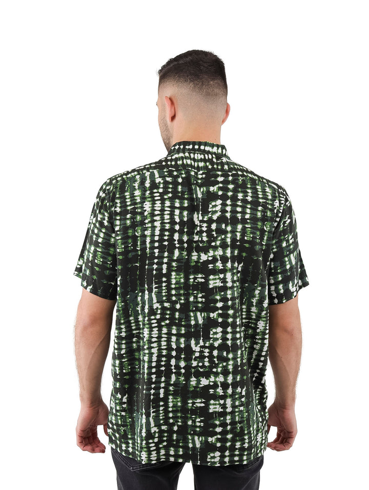 Hombre vistiendo camisa de manga corta con estampado abstracto en tonos verde, negro y blanco.