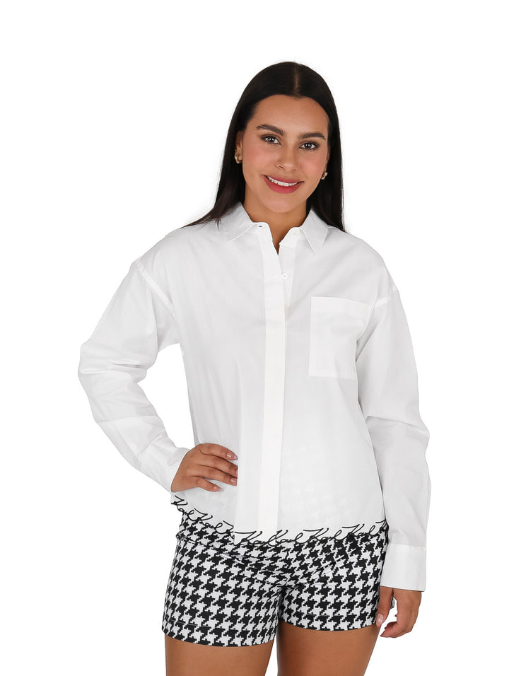 Mujer vistiendo una camisa blanca de manga larga con cuello y un bolsillo frontal.