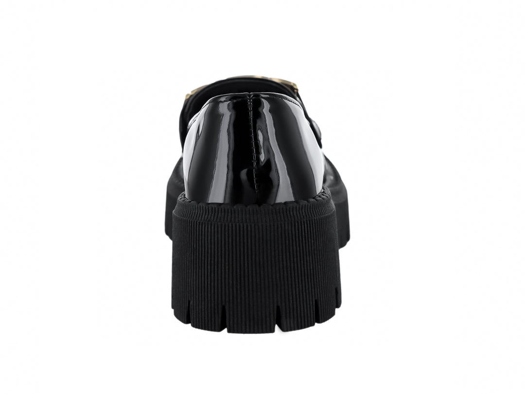 Zapato mocasín de charol negro con hebilla dorada y suela de plataforma gruesa dentada.