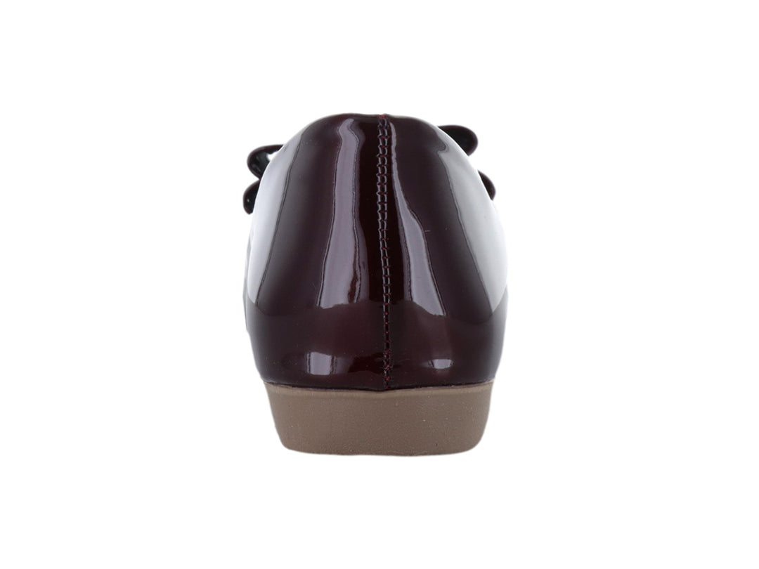 Zapato plano color vino en acabado charol brillante con detalle de moño decorativo en la parte frontal.