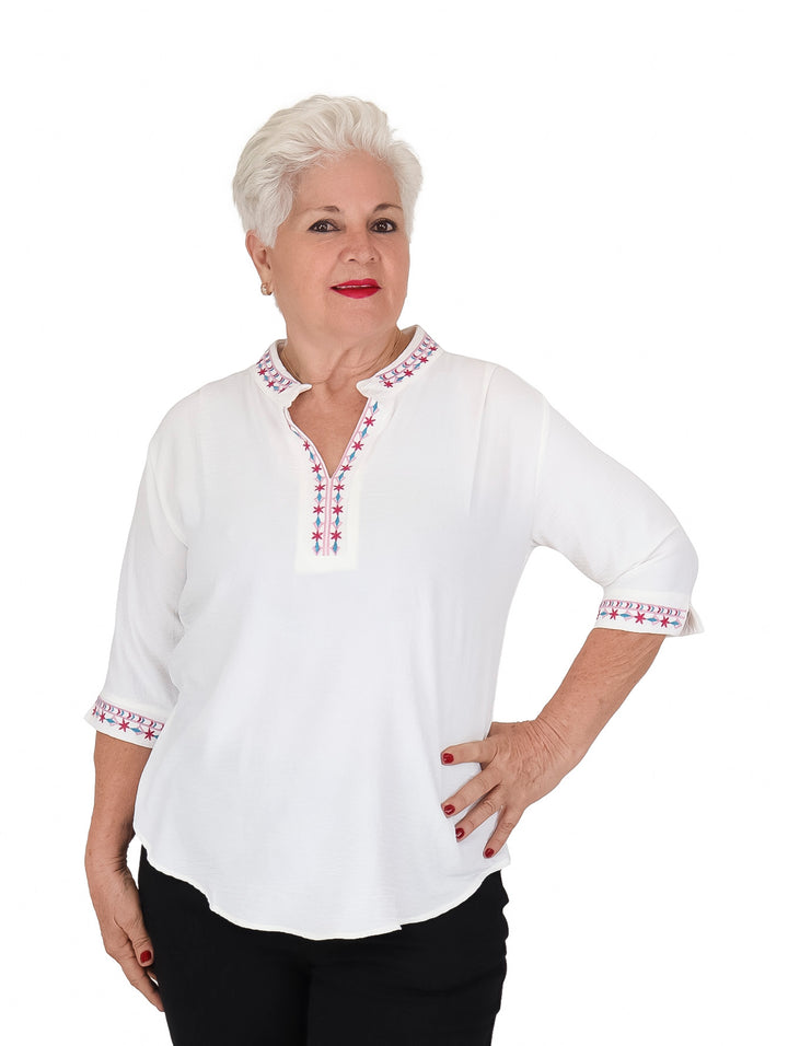 Mujer vistiendo blusa blanca de manga 3/4 con detalles bordados en rojo y azul en cuello y puños.