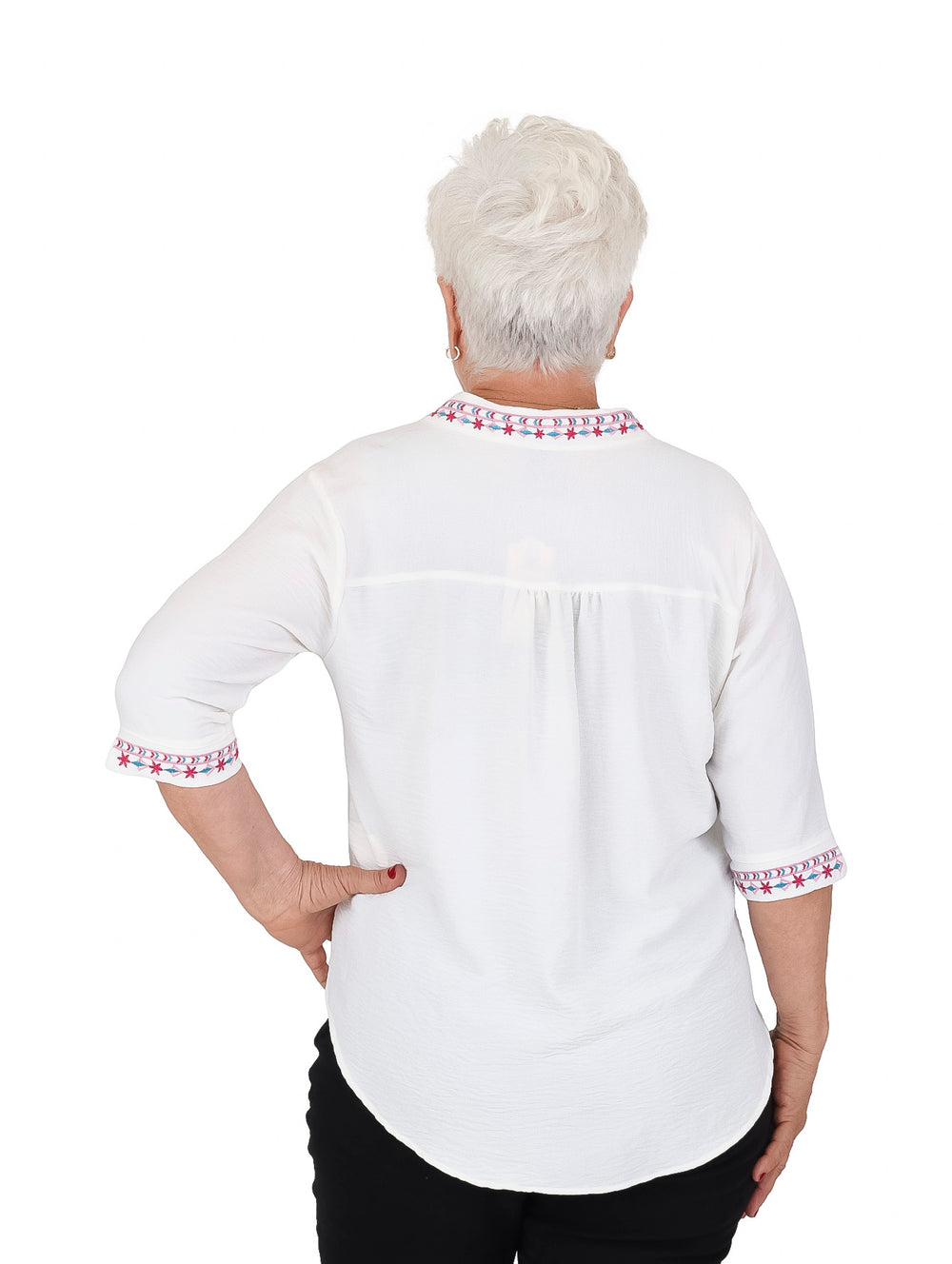 Mujer vistiendo blusa blanca de manga 3/4 con detalles bordados en rojo y azul en cuello y puños.