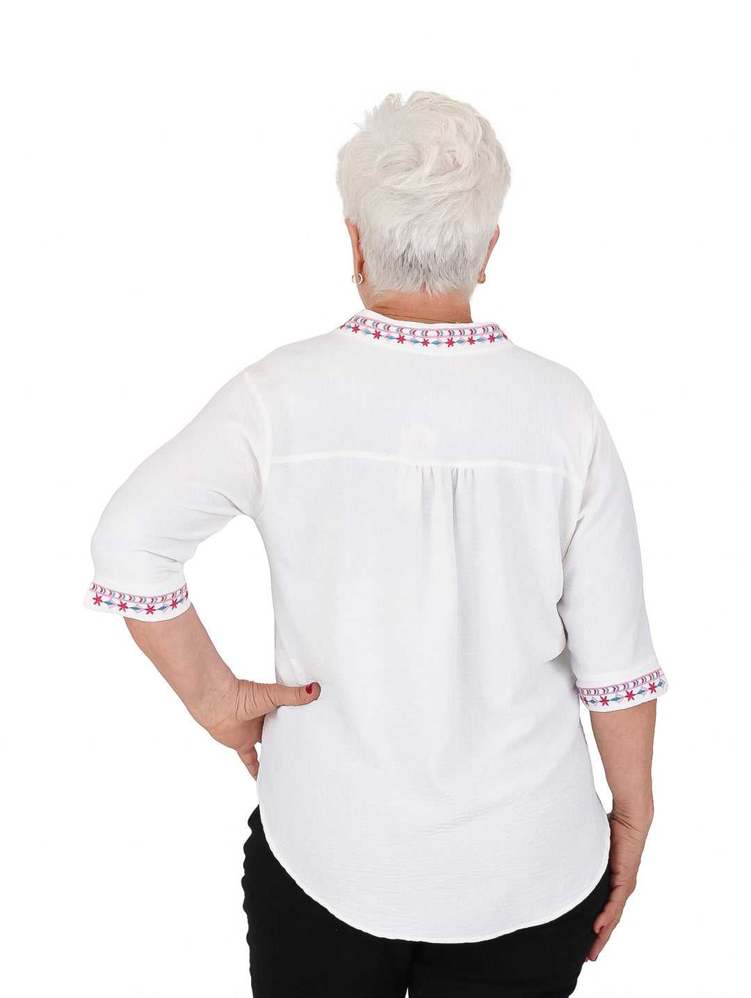 Mujer vistiendo blusa blanca de manga 3/4 con detalles bordados en rojo y azul en cuello y puños.