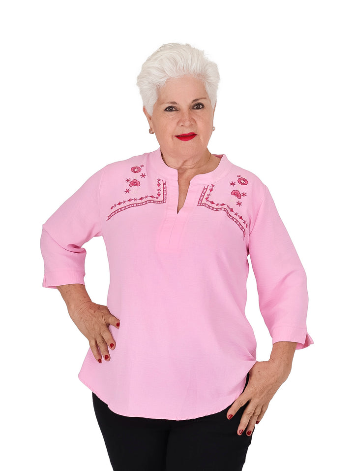 Mujer vistiendo blusa rosa de manga 3/4 con bordados florales rojos en el pecho.