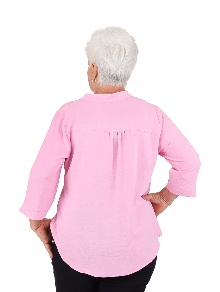 Mujer vistiendo blusa rosa de manga 3/4 con bordados florales rojos en el pecho.