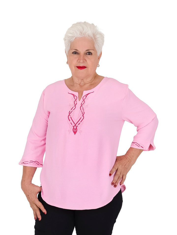 Mujer vistiendo blusa rosa de manga 3/4 con detalles bordados en el cuello y puños.