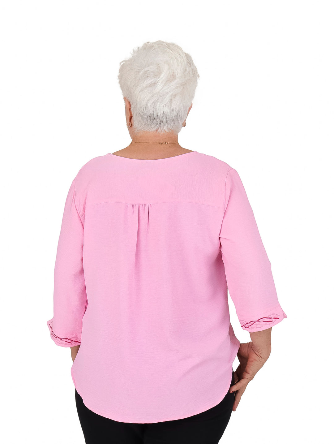 Mujer vistiendo blusa rosa de manga 3/4 con detalles bordados en el cuello y puños.