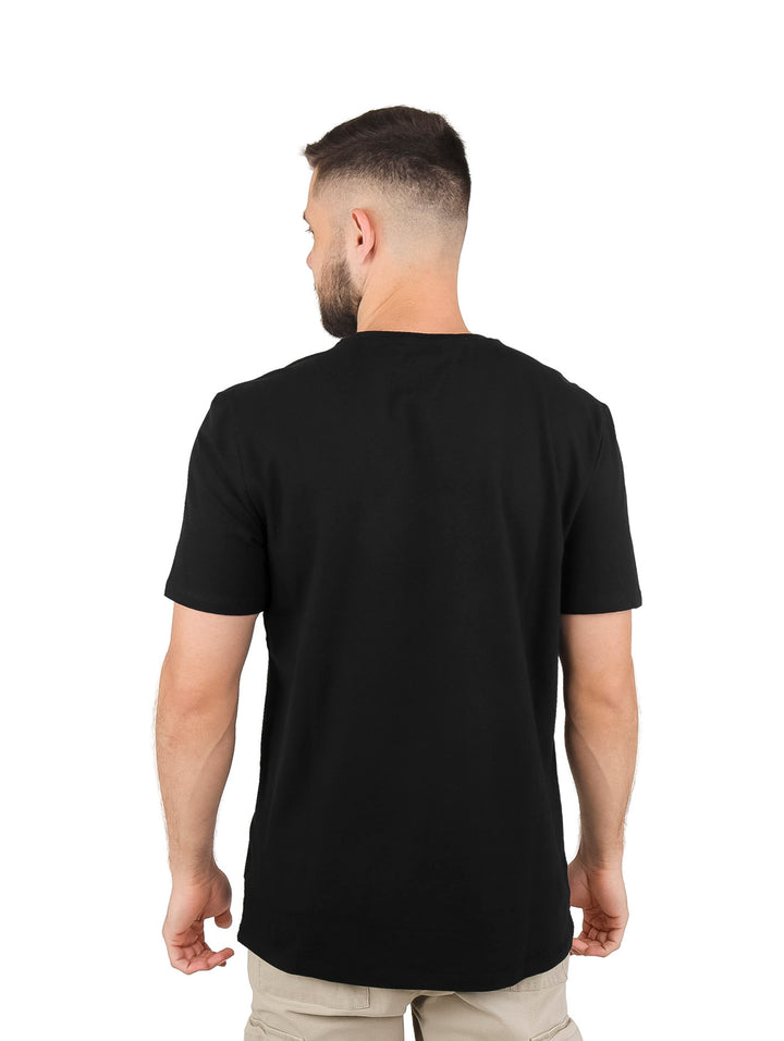 Hombre vistiendo playera negra de manga corta con logotipo DKNY estampado en colores rojo, blanco y azul.