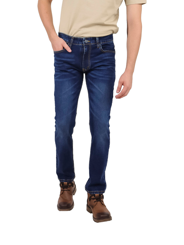 Hombre vistiendo pantalones jeans slim fit color azul oscuro, botas cafés y playera beige.