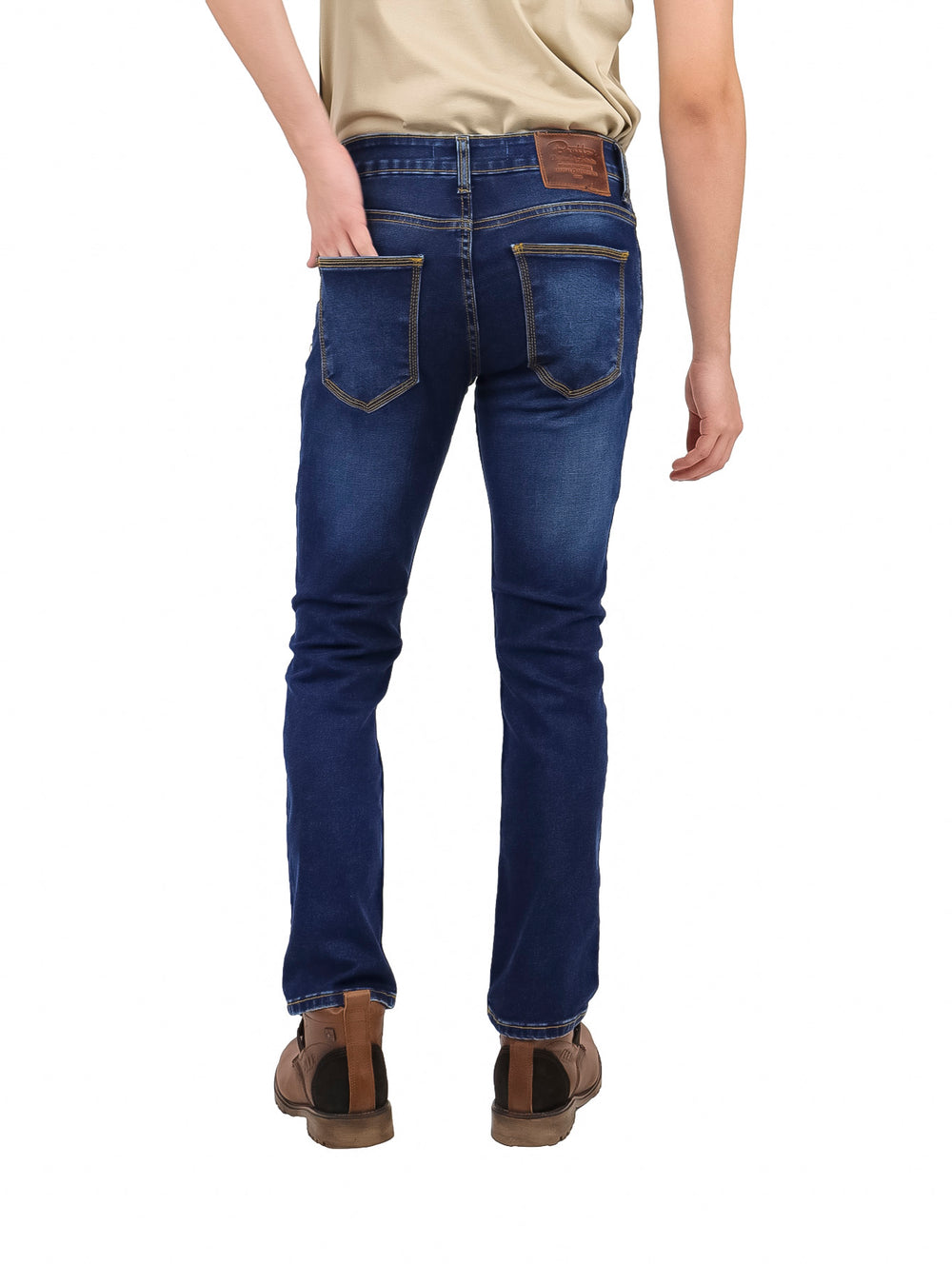 Hombre vistiendo pantalones jeans slim fit color azul oscuro, botas cafés y playera beige.