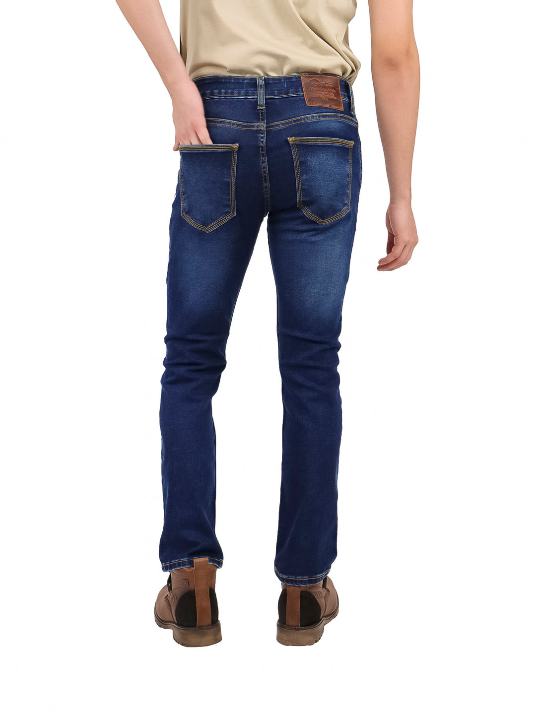Hombre vistiendo pantalones jeans slim fit color azul oscuro, botas cafés y playera beige.