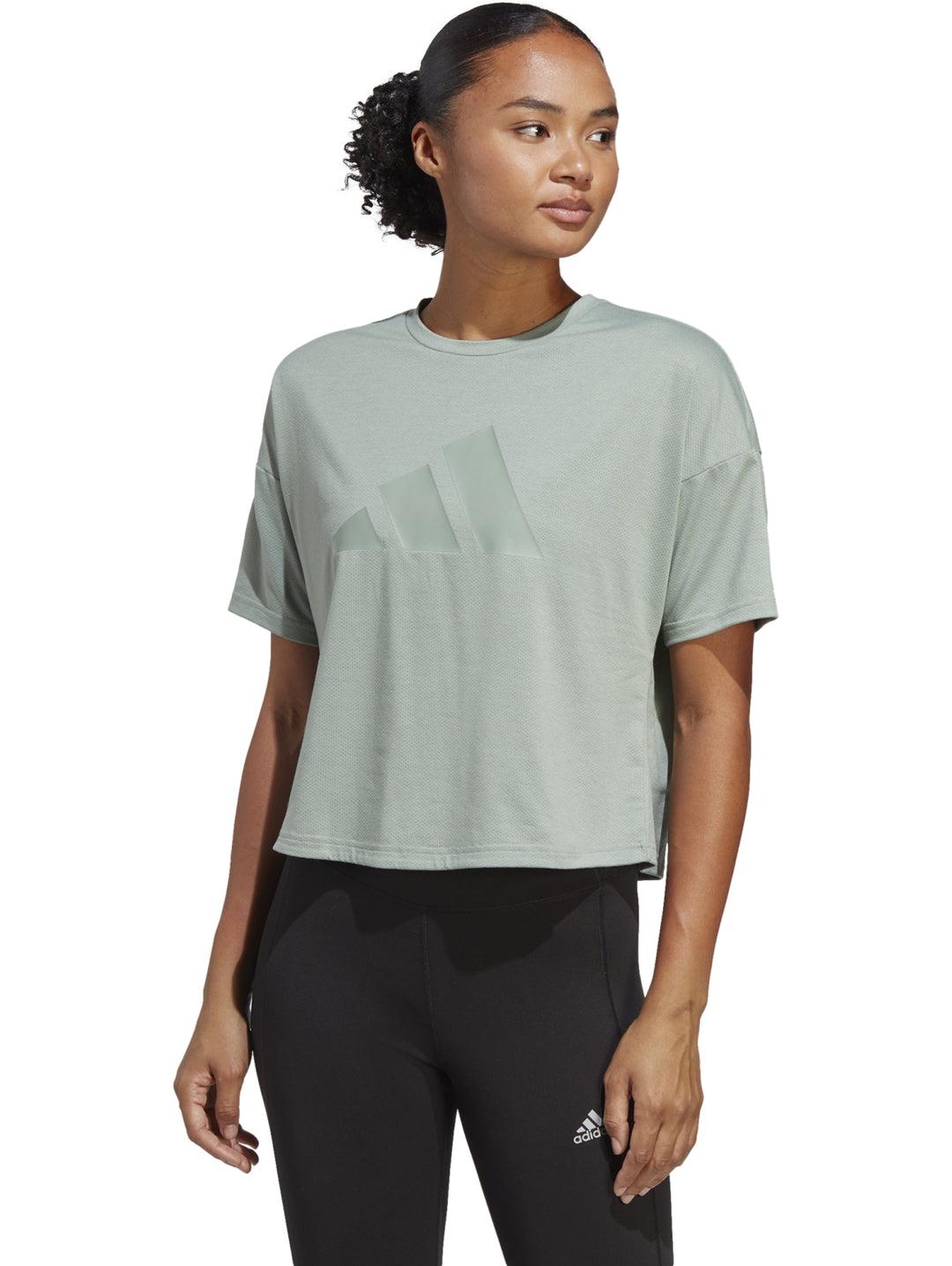 Mujer vistiendo una playera Adidas de color verde silver green con diseño de tres franjas tonales en el pecho.