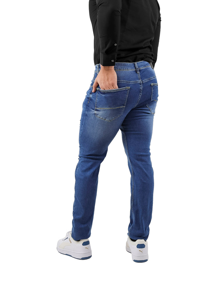 Hombre vistiendo pantalones jeans color azul con detalles rotos y calzado blanco.