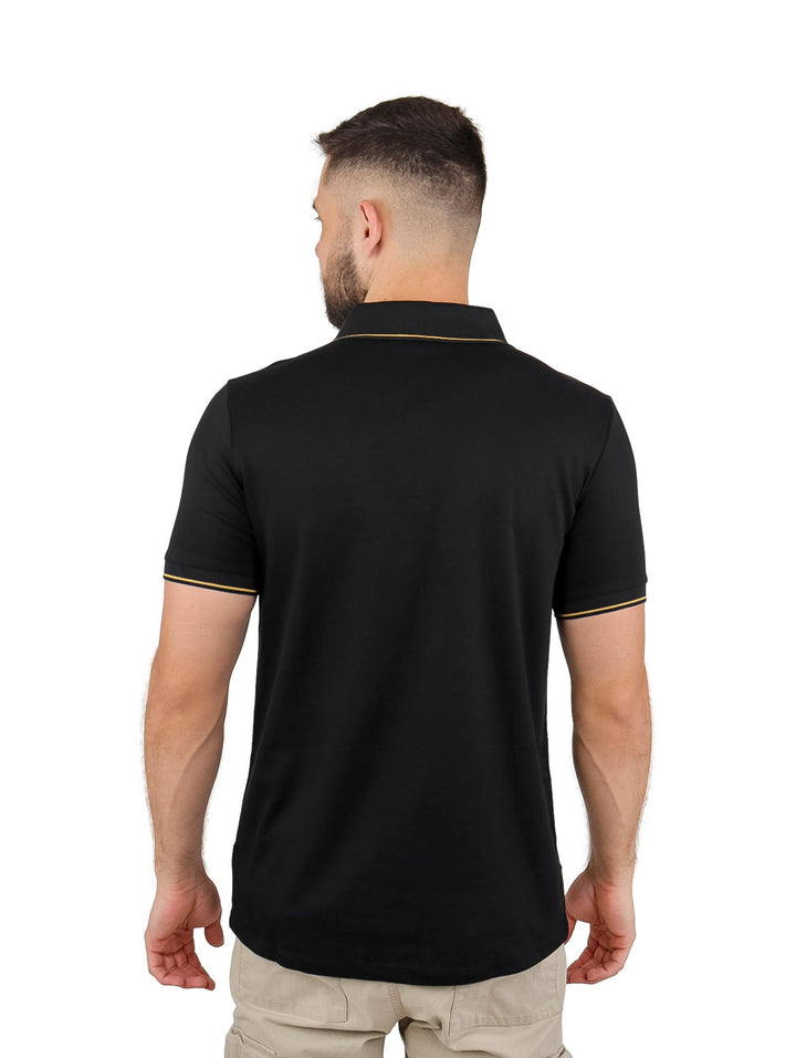 Hombre vistiendo playera polo negra con cierre y detalles en color oro en el cuello y bordes de las mangas.