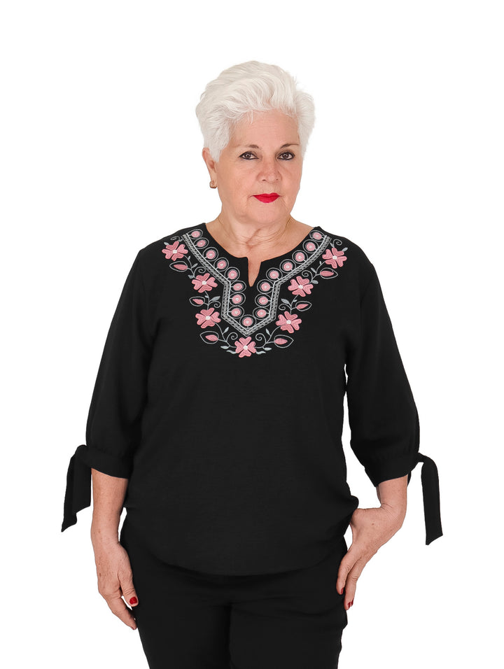 Blusa negra de manga corta con bordados florales en el cuello y moños decorativos en las mangas.