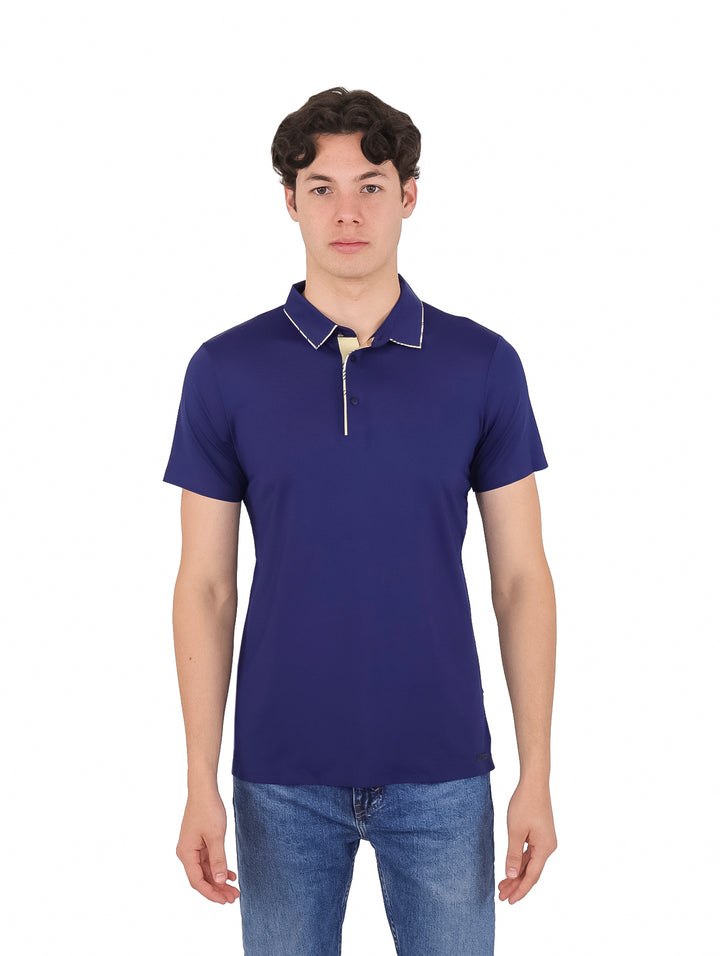 Hombre vistiendo playera polo color azul marino con detalles blancos en el cuello y jeans azules.