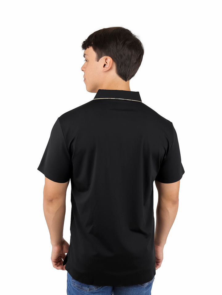 Hombre vistiendo una playera polo color negro con detalles dorados en el cuello y manga corta.