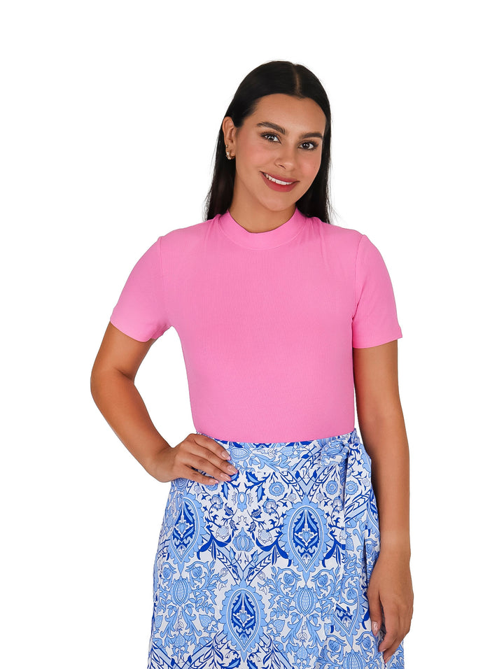 Mujer vistiendo una blusa rosa de manga corta y cuello redondo con una falda estampada en azul y blanco.