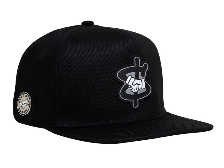 Gorra snapback color negro con visera plana y un parche bordado en el frente que muestra un apretón de manos.