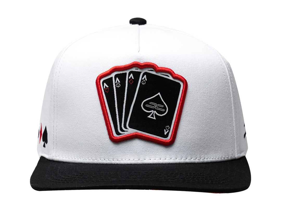 Gorra snapback blanca con visera negra y parche frontal con diseño de cartas de poker.