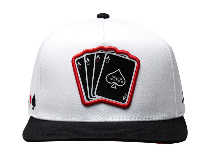 Gorra snapback blanca con visera negra y parche frontal con diseño de cartas de poker.