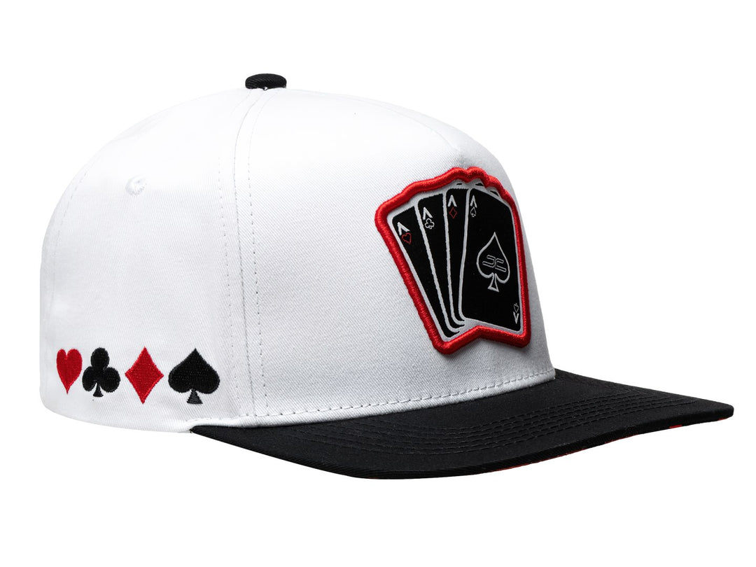 Gorra snapback blanca con visera negra y parche frontal con diseño de cartas de poker.