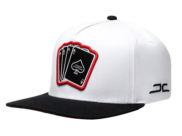 Gorra snapback blanca con visera negra y parche frontal con diseño de cartas de poker.