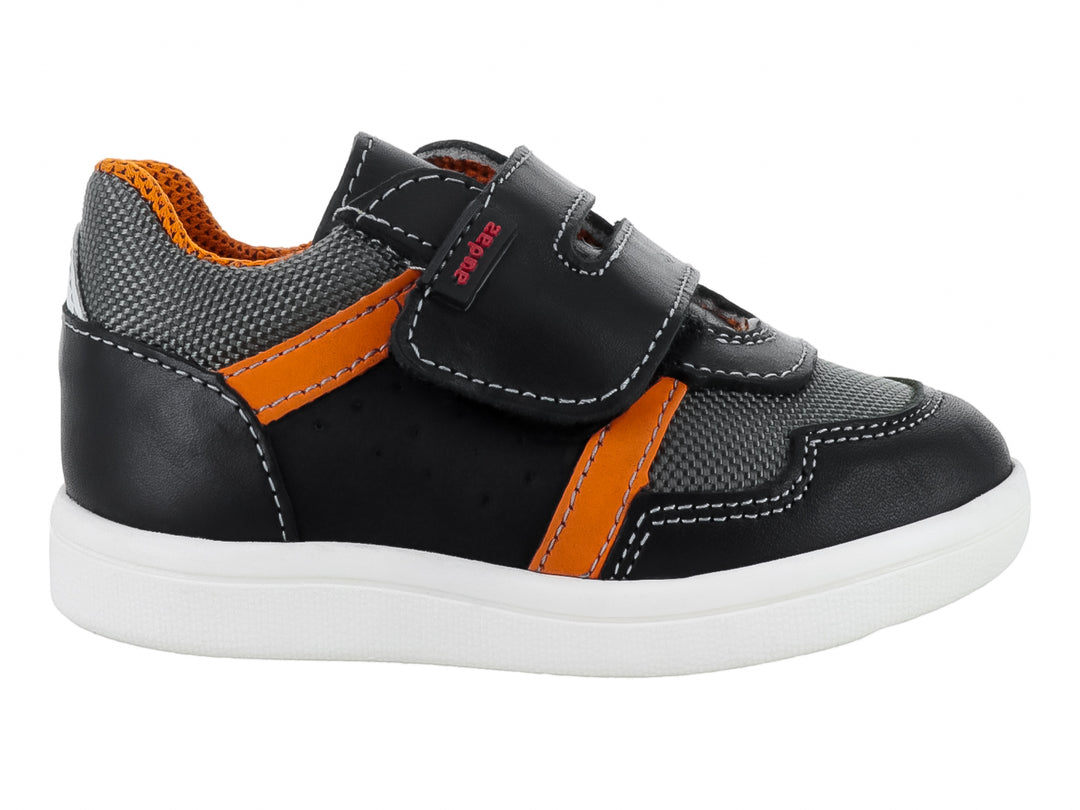Tenis infantil color negro con detalles en gris y naranja, suela blanca y cierre de velcro.
