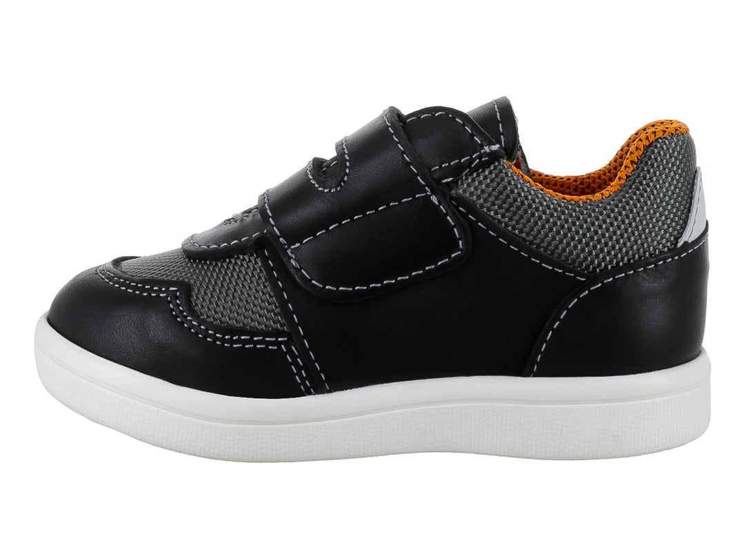 Tenis infantil color negro con detalles en gris y naranja, suela blanca y cierre de velcro.