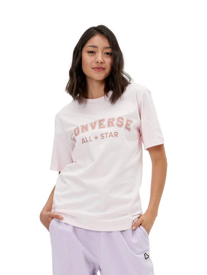 Mujer vistiendo una playera Converse de color rosa claro con logotipo en el pecho y pantalones morados.