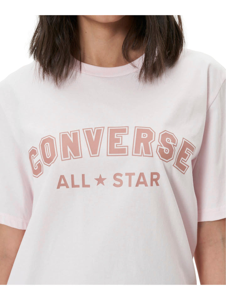 Mujer vistiendo una playera Converse de color rosa claro con logotipo en el pecho y pantalones morados.