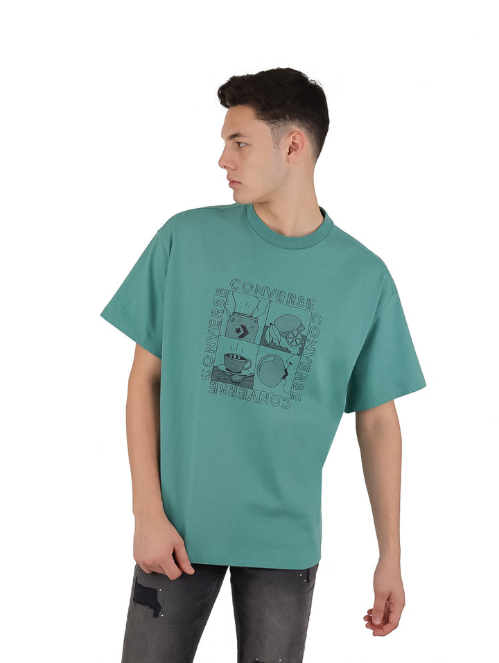 Hombre vistiendo playera Converse color verde azulado con estampado gráfico frontal y manga corta.