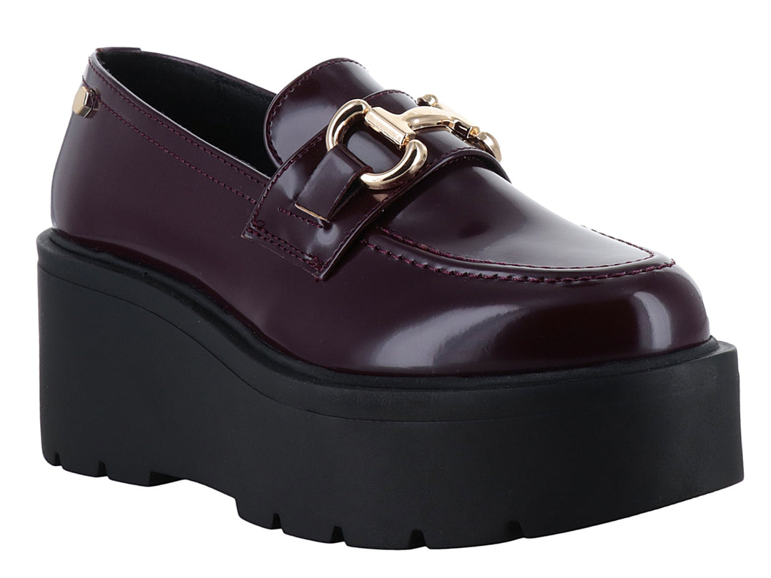 Mocasín color vino brillante con hebilla dorada y suela de plataforma negra gruesa.