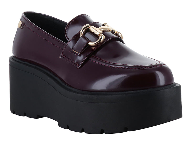 Mocasín color vino brillante con hebilla dorada y suela de plataforma negra gruesa.