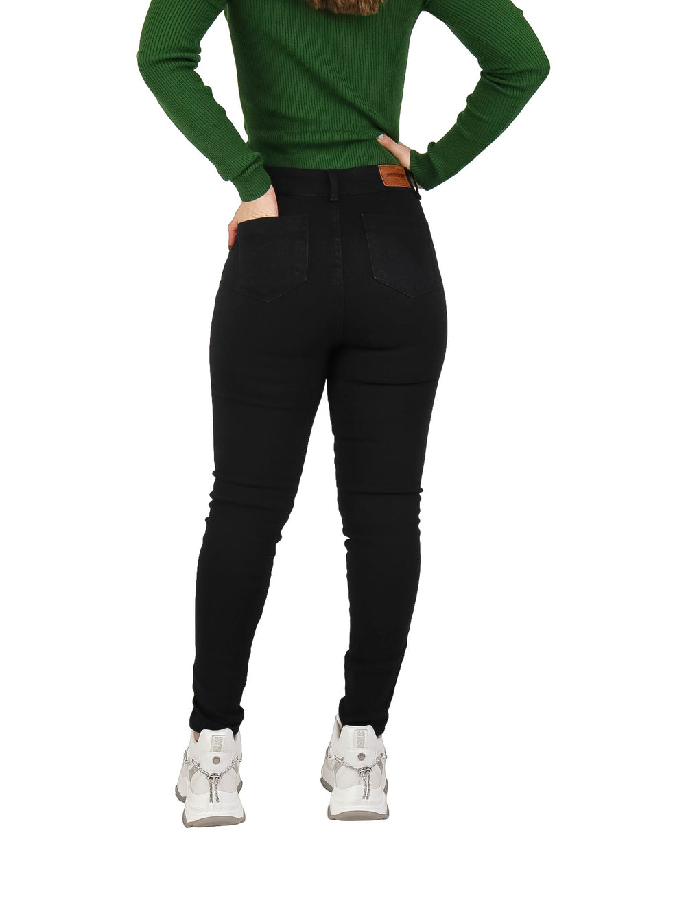 Mujer vistiendo jeans skinny negros de tiro alto, blusa verde y tenis blancos.