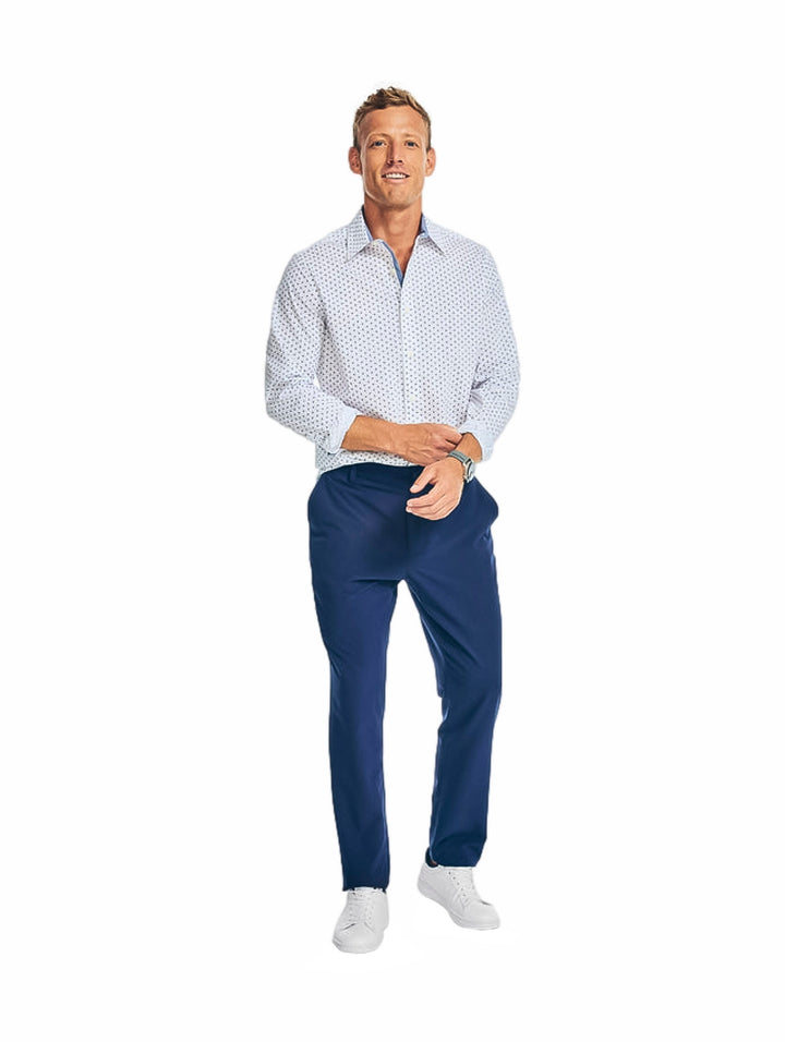 Hombre vistiendo una camisa blanca de manga larga con estampado pequeño y pantalones azules.