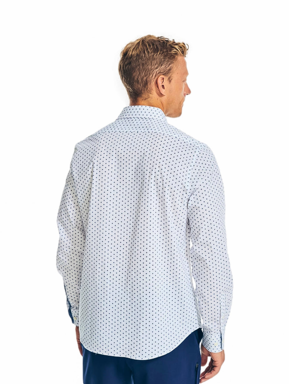 Hombre vistiendo una camisa blanca de manga larga con estampado pequeño y pantalones azules.