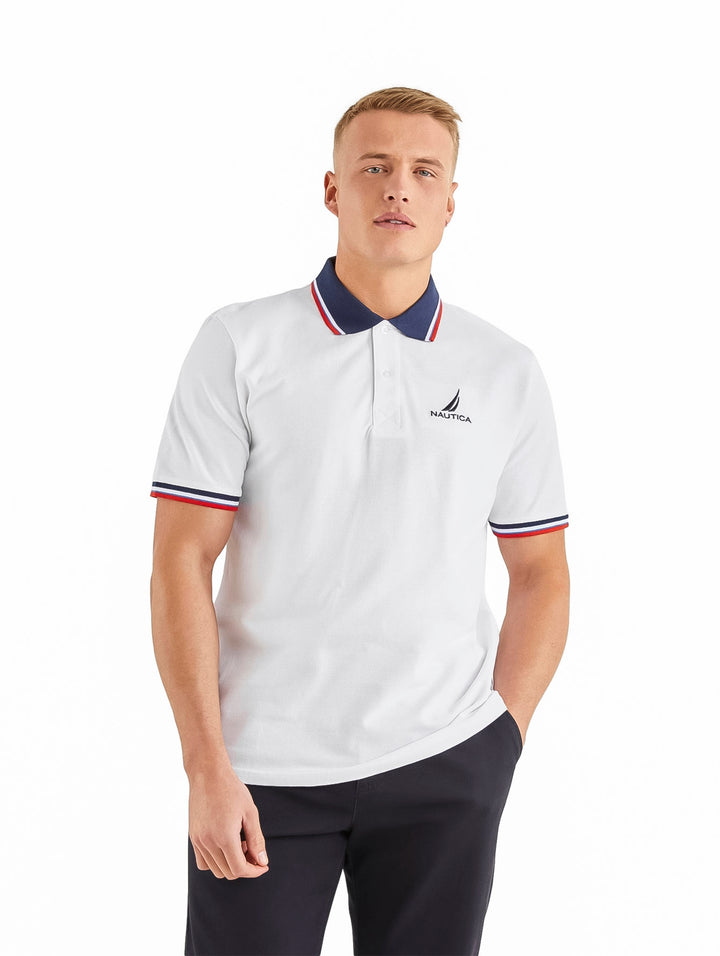 Hombre vistiendo playera polo blanca Nautica con detalles en azul y rojo en el cuello y mangas.