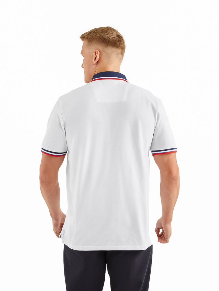 Hombre vistiendo playera polo blanca Nautica con detalles en azul y rojo en el cuello y mangas.