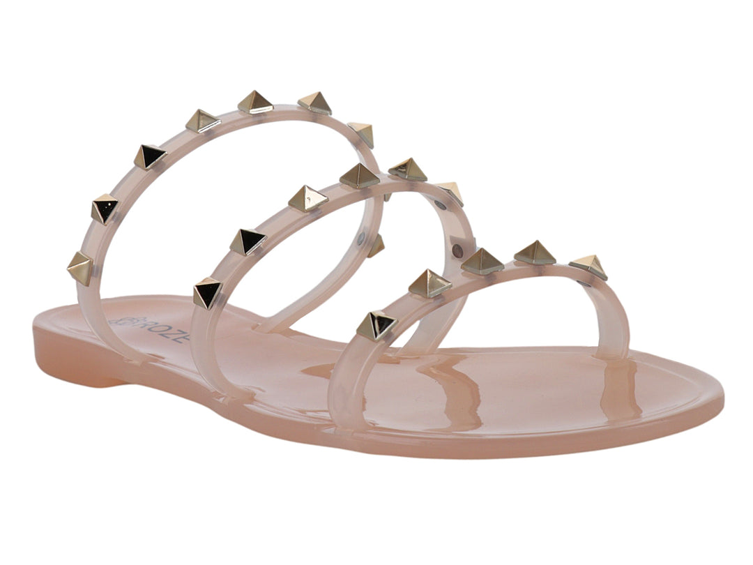 Sandalia plana color nude con tiras transparentes adornadas con tachuelas doradas.