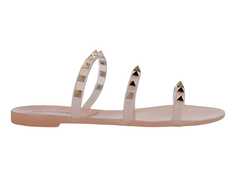 Sandalia plana color nude con tiras transparentes adornadas con tachuelas doradas.
