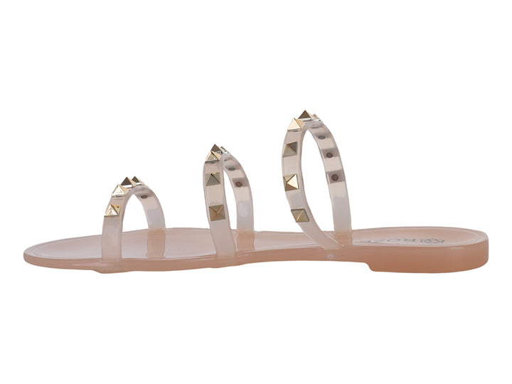 Sandalia plana color nude con tiras transparentes adornadas con tachuelas doradas.