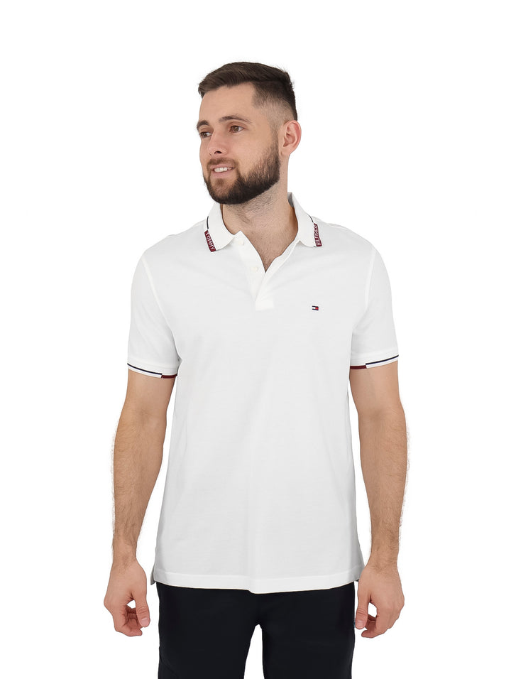 Hombre vistiendo una camiseta polo blanca de manga corta con detalles en el cuello y mangas de Tommy Hilfiger.