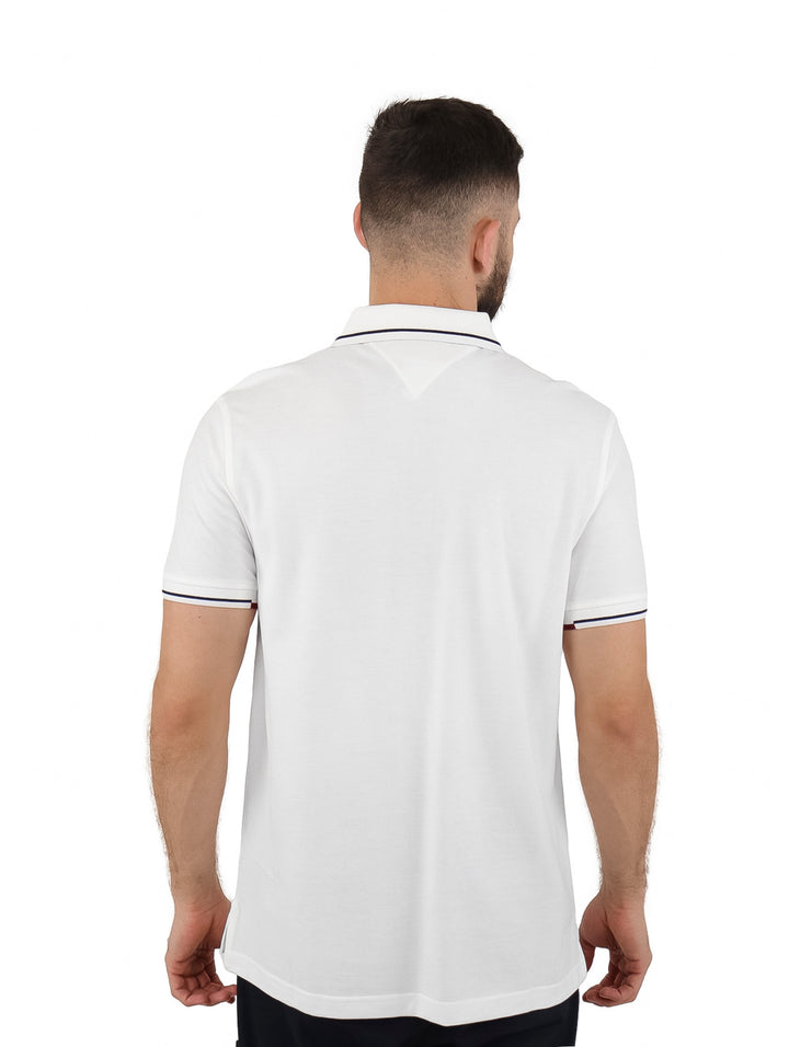 Hombre vistiendo una camiseta polo blanca de manga corta con detalles en el cuello y mangas de Tommy Hilfiger.